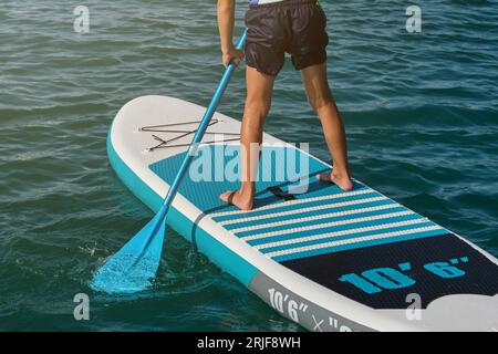 Crop Anonymous Boy steht auf SUP Board und paddelt an sonnigen Sommertagen mitten auf dem Meer Stockfoto