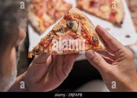 Von oben auf der Ernte anonyme Person, die ein Stück köstliche hausgemachte Pizza zu Hause isst Stockfoto
