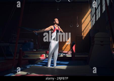 Junge Sportturnerin, die sich mit einem Gummiband im Gymnasium streckt, bevor sie ihre Übungen macht. Stockfoto