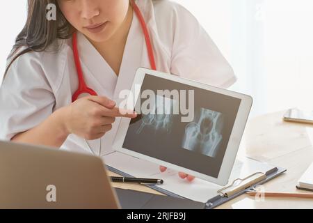 Ernten Sie anonyme Ärztin in medizinischer Uniform, die während des Online-Termins mit dem Patienten in der Klinik auf die Tablette mit dem Röntgen zeigt Stockfoto