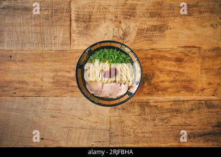 Von oben eine dekorative Schüssel mit appetitanregenden japanischen Suppe mit Nudeln und Schweinefleischscheiben in Brühe auf einem Holzschreibtisch Stockfoto