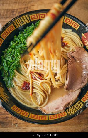 Draufsicht auf schmackhafte japanische Suppe mit gehackten grünen Zwiebeln und Schweineschnitzel in Brühe unter Nudeln auf Essstäbchen Stockfoto