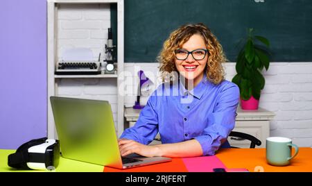 Highschool. Brillenlehrerin, die mit Notebook-Computer im Klassenzimmer arbeitet. Lehrertag. Bildung, Lernen, Lehren. Lächelnde Universität Stockfoto