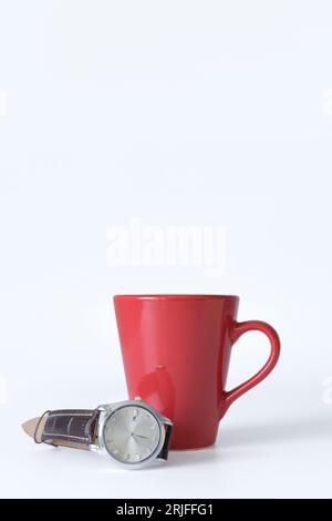 Roter Becher und Armbanduhr auf einem Armband auf weißem Hintergrund. modell, Banner vertikal. Konzept der Kaffeezeit Stockfoto