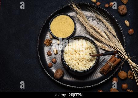 Roher und gekochter Couscous in einer schwarzen Keramikschale auf einem rustikalen schwarzen Hintergrund mit Tischoberseite Stockfoto