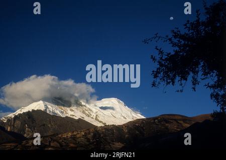 Peru, Andengebirge - Cordillera de los Andes, Cordillera Blanca. Letzte Sonnenstrahlen und aufgehender Mond über dem schneebedeckten Berg Huascarán (6768 m), Stockfoto