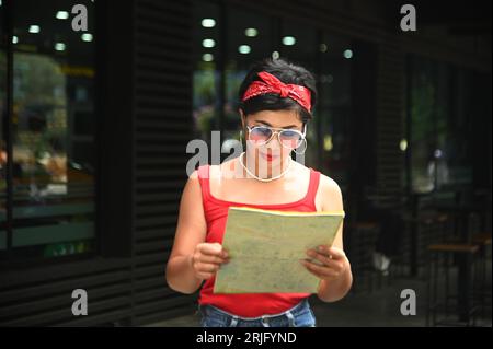 Glückliche asiatische Frau, die ein rotes T-Shirt trägt und auf die Karte blickt. Stockfoto