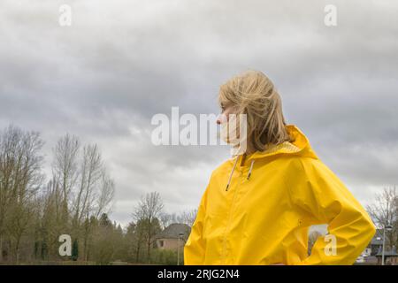 Eine junge Frau in einem gelben Regenmantel blickt auf den stürmischen Himmel. Auf Regen warten. Europäische Landschaft bei schlechtem Wetter Stockfoto