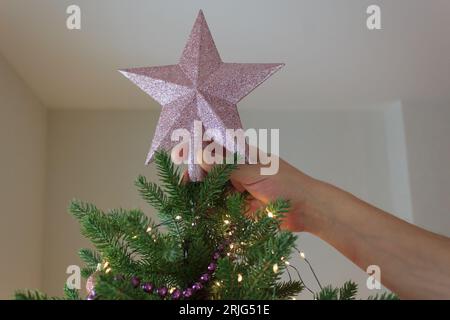 Vorbereitung auf das neue Jahr. Der Weihnachtsbaum wird von Hand mit einem festlichen Stern verziert. Stockfoto