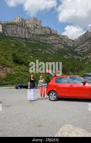 Frauen stehen in der Nähe des roten Autos in der Nähe der Talstation der Seilbahn Aeri de Montserrat im Tal des Llobregat River, Barcelona, Katalonien, Spanien. Stockfoto