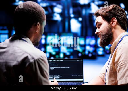Mitarbeiter aktualisieren Blade-Server und schreiben komplexe binäre Code-Skripte auf dem Laptop-Terminal. Mitarbeiter, die JavaScript, Java und Datenbankprogrammierung verwenden, um Daten mithilfe von Verschlüsselungstechniken zu schützen Stockfoto