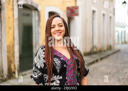 Eine Frau hockte auf einer Kopfsteinpflasterstraße. Haargeflechte und afrikanisches Kleid. Pelourinho, Brasilien. Stockfoto