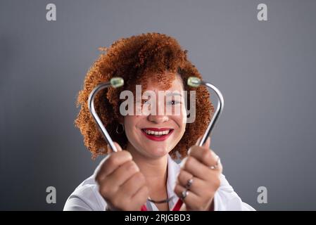 Porträt einer Tierärztin mit rotem Haar, die eine weiße Uniform trägt und ein Stethoskop nahe am Gesicht hält. Tierpflege. Isoliert auf grauem BA Stockfoto