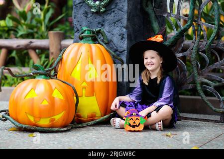 Kind in Halloween-Kostüm. Kinder tricksen oder behandeln. Kleines Mädchen als Hexe gekleidet mit Hut, der Kürbislaterne und Süßwareneimer hält. Familienfeier. Stockfoto