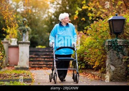 Glücklich senior Behinderte Dame mit einer Gehbehinderung, genießen Sie einen Spaziergang in einem herbstlichen Park schieben ihre Gehhilfe oder Rollstuhl. Stockfoto