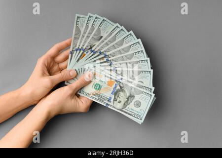 Viele Scheine von 100 Dollar in Händen sind in einem Ventilator auf einem grauen Hintergrund von oben gefaltet und bieten Platz für Text. Bargeld, Banknoten in weiblichen Händen. Stockfoto