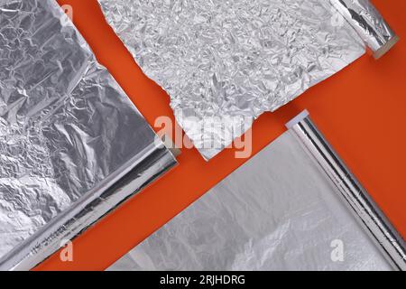 Verschiedene Rollen Aluminiumfolie auf orangem Hintergrund, flach liegend Stockfoto