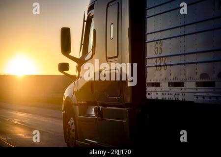 Langstreckenwagen mit 18 Rädern, die bei Sonnenaufgang oder Sonnenuntergang auf einer Autobahn fahren Stockfoto