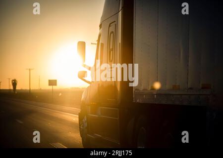 Langstreckenwagen mit 18 Rädern, die bei Sonnenaufgang oder Sonnenuntergang auf einer Autobahn fahren Stockfoto