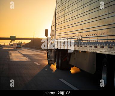 Langstreckenwagen mit 18 Rädern, die bei Sonnenaufgang oder Sonnenuntergang auf einer Autobahn fahren Stockfoto