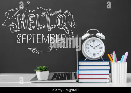 Laptop mit Wecker, Bücher und Schreibwaren auf dem Tisch in der Nähe von Tafel mit geschriebenem Text HALLO SEPTEMBER Stockfoto