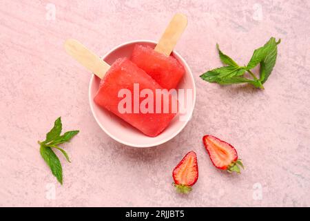 Schüssel mit Erdbeereis, frischen Beeren und Minzblättern auf rosafarbenem Grunge-Hintergrund Stockfoto