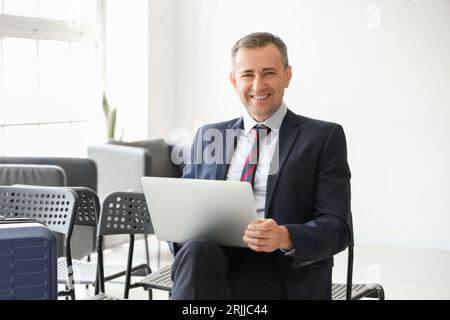 Reifer Geschäftsmann mit Laptop in der Halle des Flughafens Stockfoto
