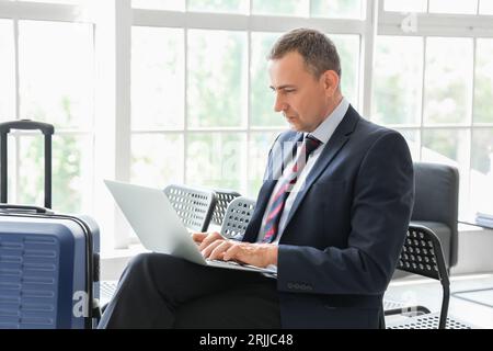 Reifer Geschäftsmann mit Laptop in der Halle des Flughafens Stockfoto