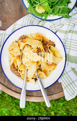 Pasta Tagliatelle Spaghetti mit cremiger Sauce, serviert auf einem Teller draußen an sonnigen Tagen. Frischer Fettucin oder Pappardelle mit Fleisch in cremiger Sauce. Stockfoto