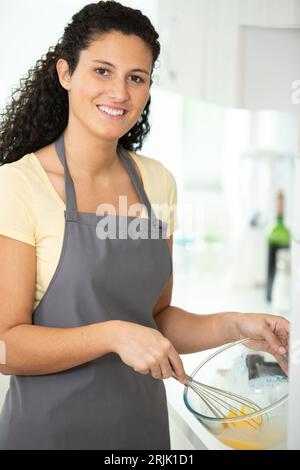 Glückliche Frau, die ein Ei in eine Schüssel knackt Stockfoto