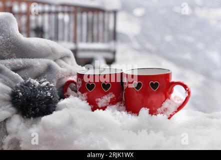 Zwei rote Tassen mit herzförmigem Motiv auf Schnee und Decke Stockfoto