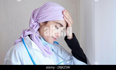 Tired Muslim doctor in hijab looking out window takes off mask Stockfoto