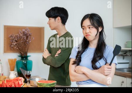 Unhappy and angry young Asian couple ignoring each other, feeling depressed and disappointed after arguing while cooking in the kitchen together. Stockfoto