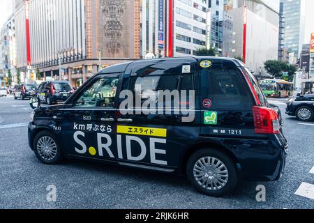 Tokyo, Japan - August 22 2023: Taxi across the famous Ginza Shopping District intersection in Tokyo. Translation: If you call KM; Excellent; Wireless. Stock Photo