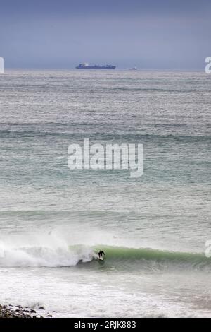 Bild von Tim Cuff - 20. Mai 2023 - Ein Surfer macht das Beste aus dem großen Anstieg in Cable Bay. Das schlechte Wetter brachte das kaputte Schiff Shiling ins Sichtfeld Stockfoto