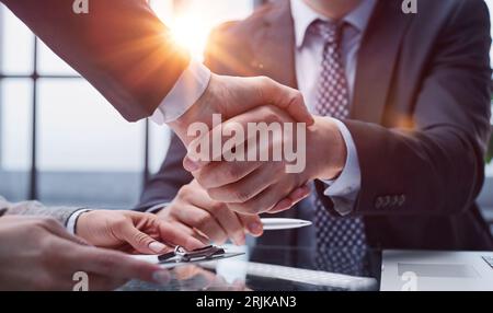 Geschäftsleute oder Anwälte schütteln sich die Hand, wenn sie ein Meeting oder eine Verhandlung in einem sonnigen Büro beenden. Stockfoto