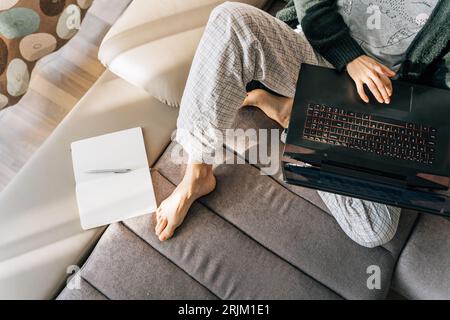 Draufsicht auf eine Frau im Schlafanzug mit Laptop und Notizblock. Stockfoto