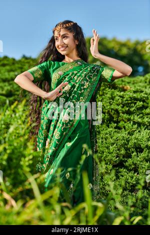 Unbekümmerte junge indianerin im traditionellen Sari-Tanz, während sie in der Nähe von Pflanzen im Park steht Stockfoto