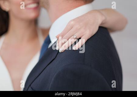 Eine Frau, die mit einem Ring am Finger lächelt und ihre Hand sanft auf die Schulter eines Mannes legt. Stockfoto