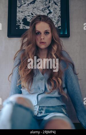Eine Frau in blauem Pullover und Jeans, die an eine Wand lehnt Stockfoto