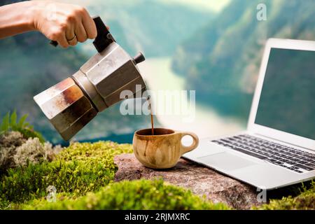 Der Morgenkaffee eines Freelancers mit digitalem Nomaden, einer Moka-Kaffeemaschine, einer traditionellen finnischen Holztasse Kuksa und einem Laptop vor skandinavischer Kulisse Stockfoto