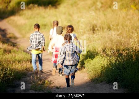 Fröhliche und begeisterte kleine Jungen und Mädchen, Kinder in lässiger Kleidung, die auf der Wiese laufen und die Natur an warmen, sonnigen Tagen erkunden Stockfoto