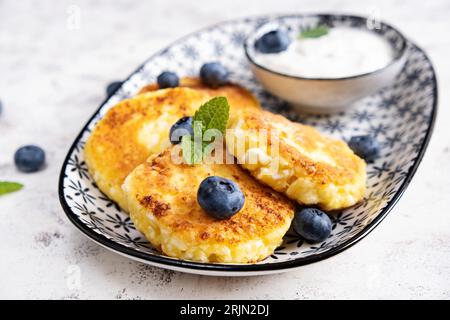 Hüttenkäse-Pfannkuchen mit Sauerrahm und Heidelbeeren auf hellem Hintergrund. Frühstück oder Mittagessen Stockfoto
