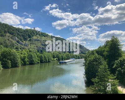 Ein ruhiger Blick auf ein großes Boot, das auf dem Fluss entlang eines Berges segelt, umgeben von üppigen Bäumen Stockfoto