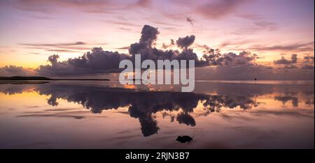 Ein ruhiger rosa Sonnenuntergang mit großen flauschigen Wolken über dem Meer, die sich auf dem Wasser spiegeln Stockfoto