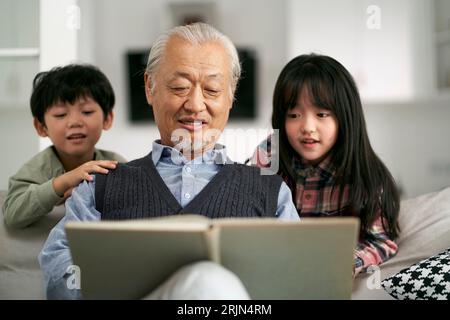 Seniorengroßvater aus Asien hat sich mit zwei Enkeln zu Hause amüsiert Stockfoto