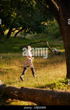 Kleines aktives Kind, Mädchen in lässigen Kleidern, laufend, spielend auf Wiese im Wald an warmen sonnigen Tagen Stockfoto