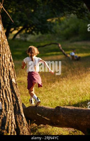 Kleines aktives Kind, Mädchen in lässigen Kleidern, laufend, spielend auf Wiese im Wald an warmen sonnigen Tagen Stockfoto