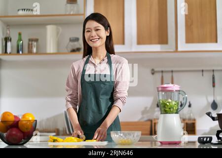 Glückliche junge asiatische Hausfrau, die in der Küche steht und die Kamera lächelt Stockfoto
