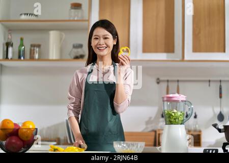 Glückliche junge asiatische Hausfrau, die in der Küche steht und die Kamera lächelt Stockfoto